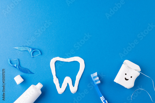 Image of toothbrush, toothpaste, string, liquid and tooth made of paste on blue surface