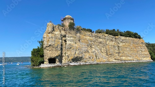 island in the Bolsena lake on a sunny summer day in the Lazio region of Italy with blue sky and rocky cliff