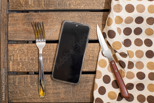 tenedor, servilleta y cuchillo, en vez de plato movil. Concepto tecnología y movil alimentación, movil en las comidas, influencia de las redes sociales en la forma de alimentarnos.