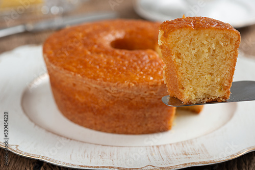 Homemade round cornmeal cake, typical Brazilian food made from corn in a June party and dish on a rustic wooden table with selective focus on the slice on the spatula