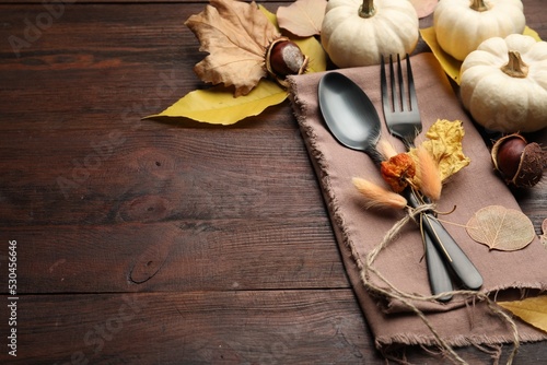 Seasonal table setting, space for text. Cutlery with pumpkins and autumn leaves on wooden background