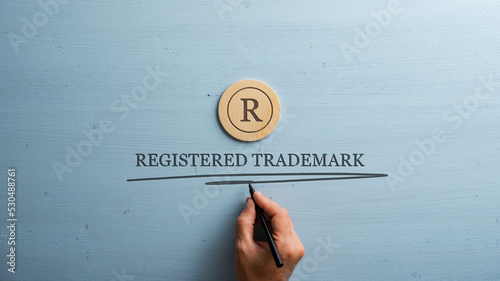 Letter R cut into wooden cut circle and male hand writing a Registered trademark sign under it