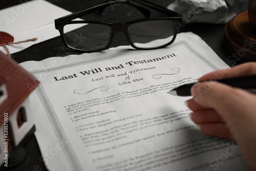Woman signing last will and testament at black table, closeup