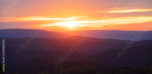 Bright red-orange dawn over a misty mountain forest. Evening landscape on the sunset sky over the Siberian taiga. Colorful sky at foggy morning at sunrise above coniferous forest in mountain
