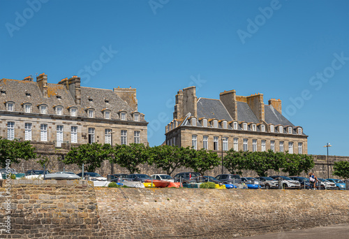 St. Malo, Brittany, France - July 8, 2022: Manions and palaces along Rue D'Orleans reaching Bastion Saint Louis under blue sky. Paking with cars add colors.