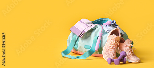 Bag with sportswear and equipment on yellow background