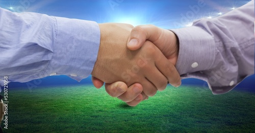 Composition of two businessmen shaking hands over sports stadium
