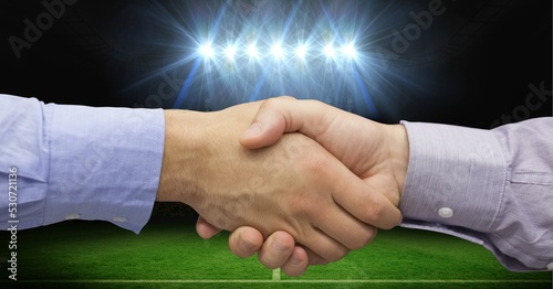 Composition of two businessmen shaking hands over sports stadium