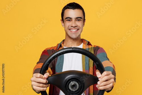 Young smiling fun middle eastern man 20s he wear casual shirt white t-shirt pretending driving hold in hand steering wheel isolated on plain yellow background studio portrait People lifestyle concept.