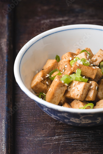 Fried tofu with sesame seeds, green onion and spices on the wooden vintage background. Homemade healthy vegetarian Asia and Japanese dish - fried tofu, close up