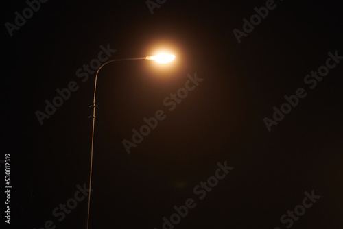 One night lamppost shines with faint mysterious yellow light through evening fog, copy space