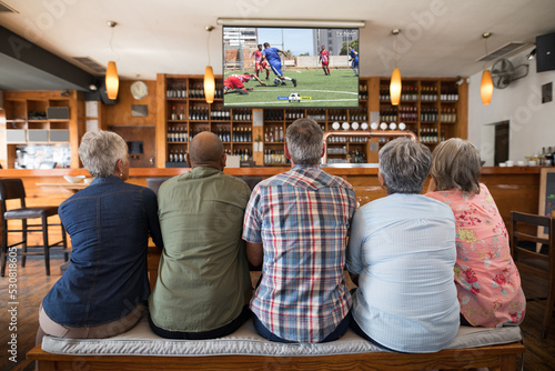 Senior diverse friends supporting and watching tv in bar with football match on screen