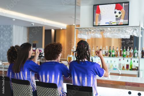 Diverse friends supporting and watching tv in bar with football match on screen