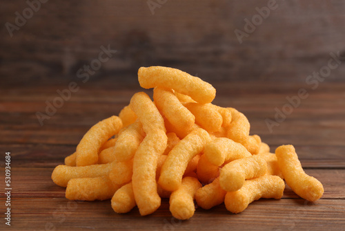 Heap of tasty cheesy corn puffs on wooden table
