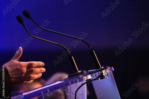 focus sur un micro et les mains d'un orateur prononçant un discours à la tribune lors d'un meeting politique, d'un colloque ou d'une réunion 