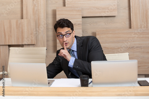 Young cunning employee in black suit working in the office and stealing information from laptop of his colleague