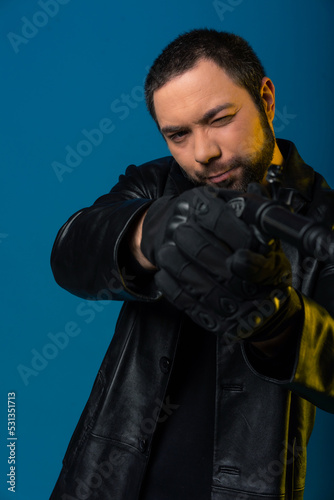 portrait of a man in a black leather coat. a model with a beard on a blue background is aiming with a gun. black hair on head