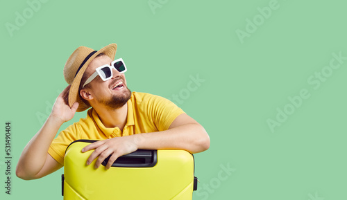 Wide narrow shot of funny smiling young man in summer hat and sunglasses with suitcases dream of vacation or trip. Happy male traveler imagine good holidays. Copy space. Travel and tourism concept.
