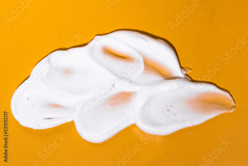 White cosmetic cream lotion smears on bright orange background top view.