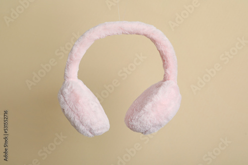 Fluffy earmuffs on beige background. Stylish winter accessory