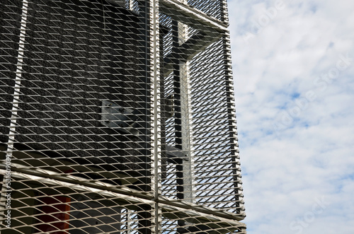 steel cladding of a building with a expanded metal lattice structure. galvanized gray nets protect the industrial building. Blue sky in contrast to a silver background, wall