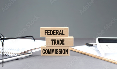 FTC -FEDERAL TRADE COMMISSION text on wooden block with notebook,chart and calculator, grey background