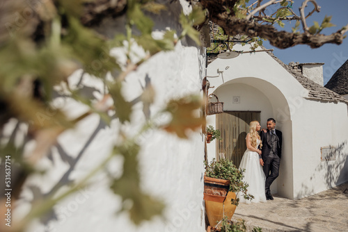 Portrait of wedding couple standing under arch of old white stone dwelling trullo with conical roof, talking. Wedding.