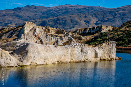 Quartz gravel cliffs reflected in the Blue Lake near the old mining town of St Bathans in the Central Otago region of the South Island of New Zealand