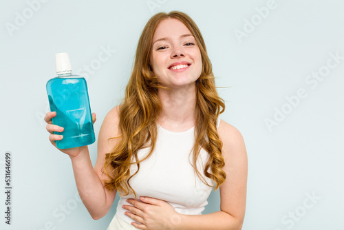 Young caucasian woman holding a mouthwash isolated on blue background laughing and having fun.