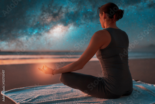 silhouette of a woman on the beach outdoors meditating at night with stars and milky way in the background 