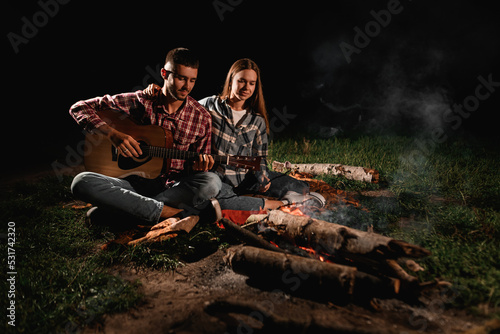 Lovely couple with guitar spending time together at park at evening by the fire.
