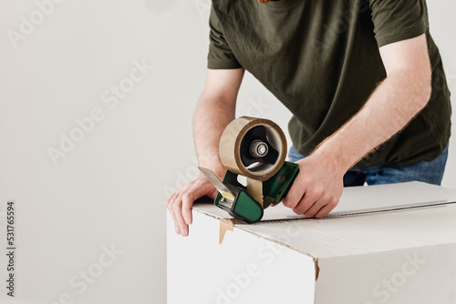Detalle de un hombre usando una herramienta para precintar una caja de cartón con cinta adhesiva marrón. Embalaje de cajas de mudanza.