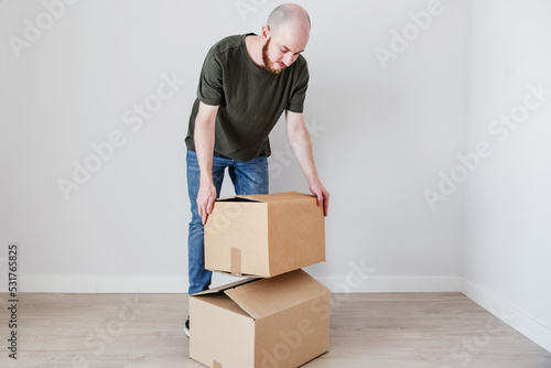 Un hombre joven con barba agarra una caja de cartón. Concepto de mudanza y amueblar un nuevo hogar.