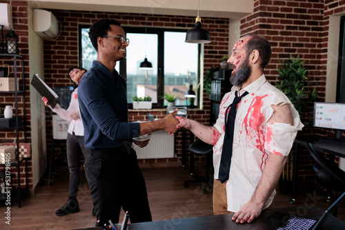 Businessman doing handshake with evil zombie, having conversation with brain eating corpse in startup office. Undead scary monster with bloody wounds saluting person, sinister devil.
