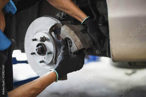 Auto mechanic installing car front brake caliper and brake pads.