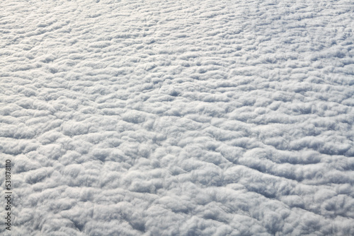 Breathtaking over clouds view from aircraft window, thick white blue clouds looks like soft foam, overcast with fresh frosty air. Beautiful cloudy sky view to troposphere, heavy cloudiness