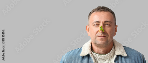 Ill mature man with clothespin on his nose against grey background with space for text