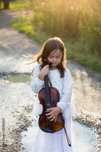 Dziewczynka ze skrzypcami w ręku stoi na dworze i włosy rozwiewa jej wiatr