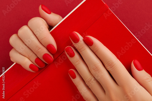 Female hand with manicure holding notepad. Red matt nail design