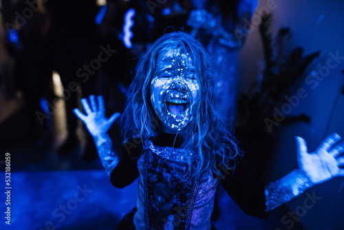 Portrait of a smiling girl at a children's party. Fluorescent paint on the face in ultraviolet light. Film noise. Diffuse focus