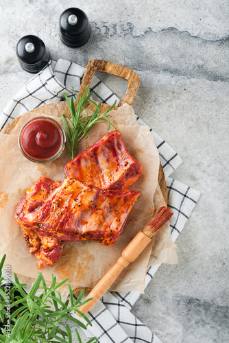 Pork ribs. Raw meat. Raw pork ribs in marinade with spices, rosemary, tomato sauce and garlic on old wooden stand on black stone table background. Barbecue concept. Top view. Mock up.