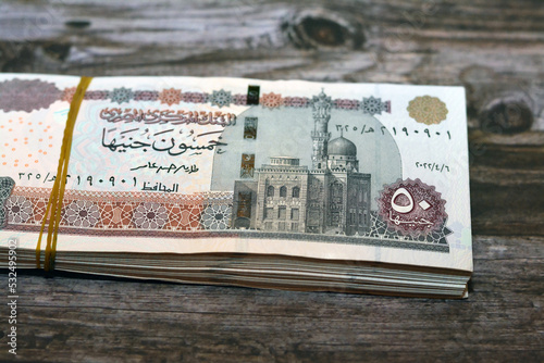 A pile of Egyptian money banknotes of 50 LE fifty pounds series 2022 features Abu Hurayba Mosque on obverse and image of temple of Edfu, winged scarab and a pharaonic boat on reverse isolated on wood