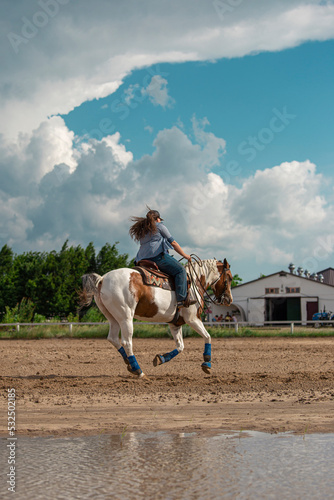 Horse rider near the water. Horse loping in the arena. Pinto horse near the water.