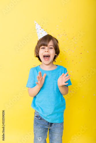 Handsome Little birthday boy in blue shirt and hat with balloons, yellow background, happy birthday