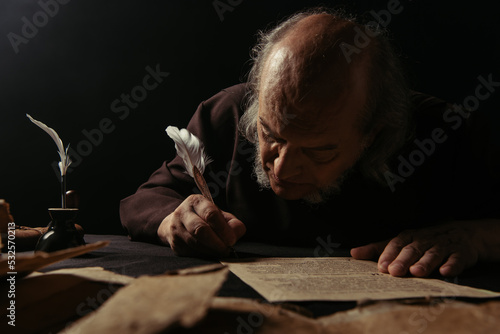 senior abbot writing manuscript on parchment isolated on black.