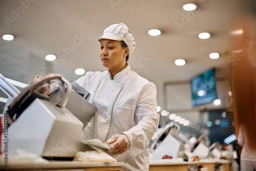 Supermarket clerk using slicer while working at delicatessen section.