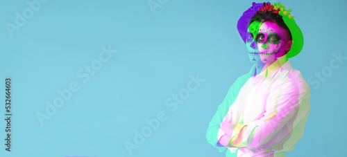 Young man with painted skull on his face for Mexico's Day of the Dead (El Dia de Muertos) against light blue background with space for text