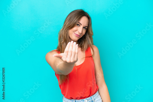 Young caucasian woman isolated on blue background inviting to come with hand. Happy that you came