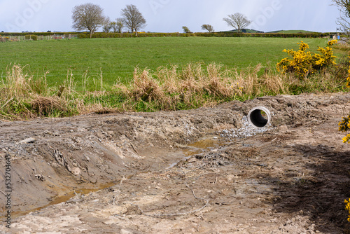 A drainage ditch is dug in a field, with a small culvert pipe to drain water into a small stream.