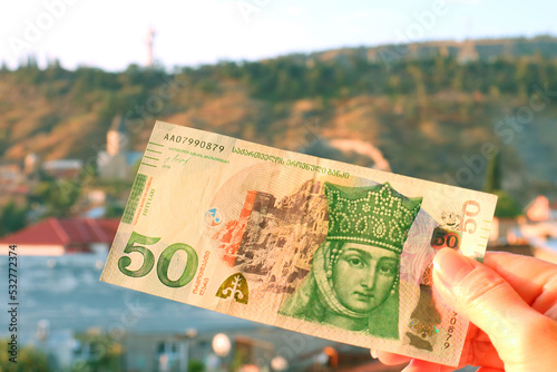 50 Georgian Lari Banknotes in Obverse Side in Hand with Blurry Tbilisi City View in Backdrop